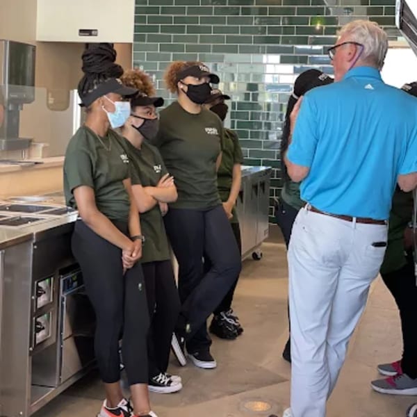 Fresh Green staff in green shirts and masks listening to a man in a blue polo shirt.