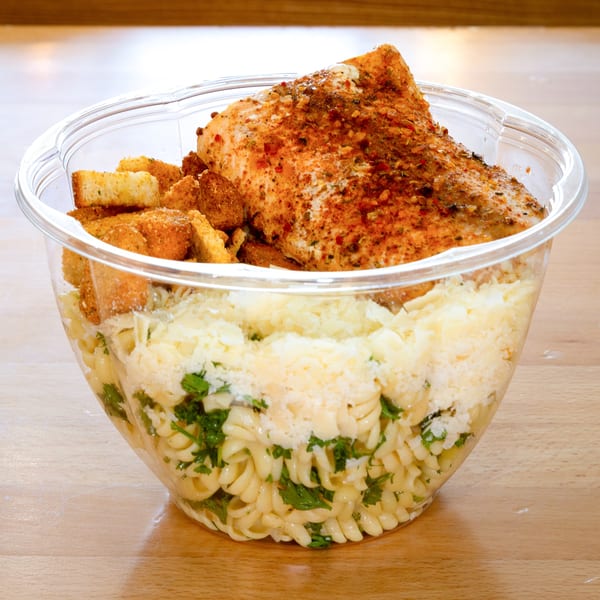 Fresh Green's pasta salad with grilled chicken, croutons, and parmesan cheese in a clear bowl.