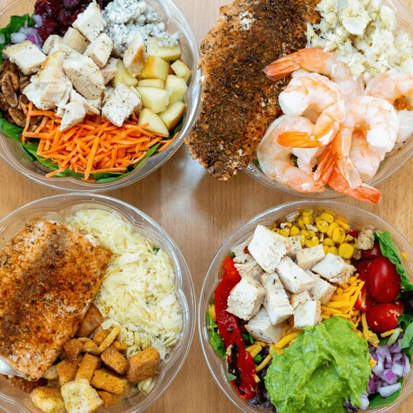 Four Fresh Green salads in clear plastic bowls, featuring chicken, salmon, and shrimp.