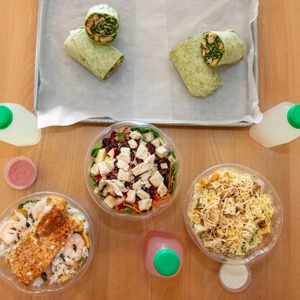 Overhead view of Fresh Green wraps, salads with chicken, salmon, and shrimp, and drinks on a wooden table.