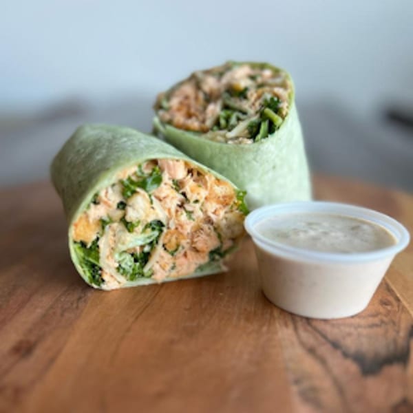 Two Fresh Green buffalo chicken wraps with green tortillas and a side of dipping sauce on a wooden board.