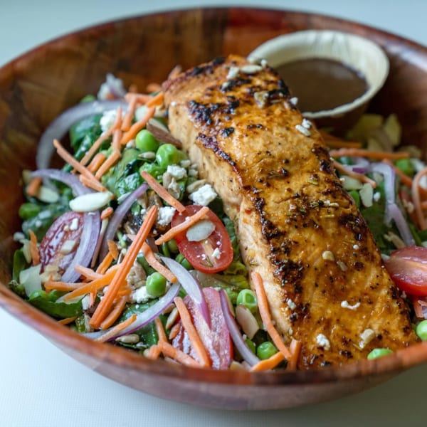 Fresh Green salmon salad with spinach, carrots, onions, peas, tomatoes, and dressing in a wooden bowl.