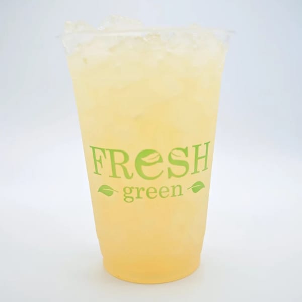 Iced lemonade in a clear plastic cup with the Fresh Green logo on a white background.