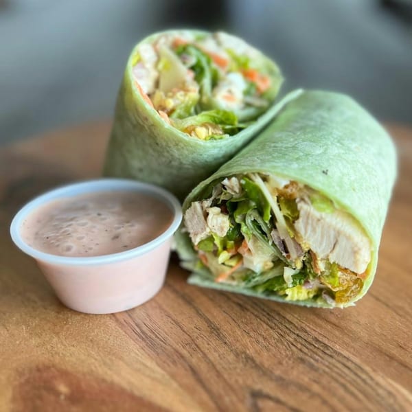 Two Fresh Green wraps filled with chicken, lettuce, and vegetables, with a side of dressing.