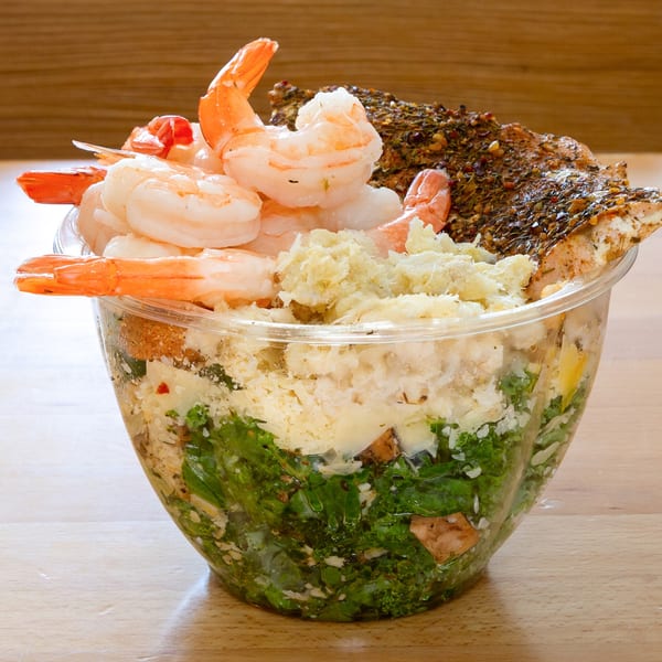 Fresh Green salad with shrimp, salmon, and shredded cheese in a clear plastic bowl.